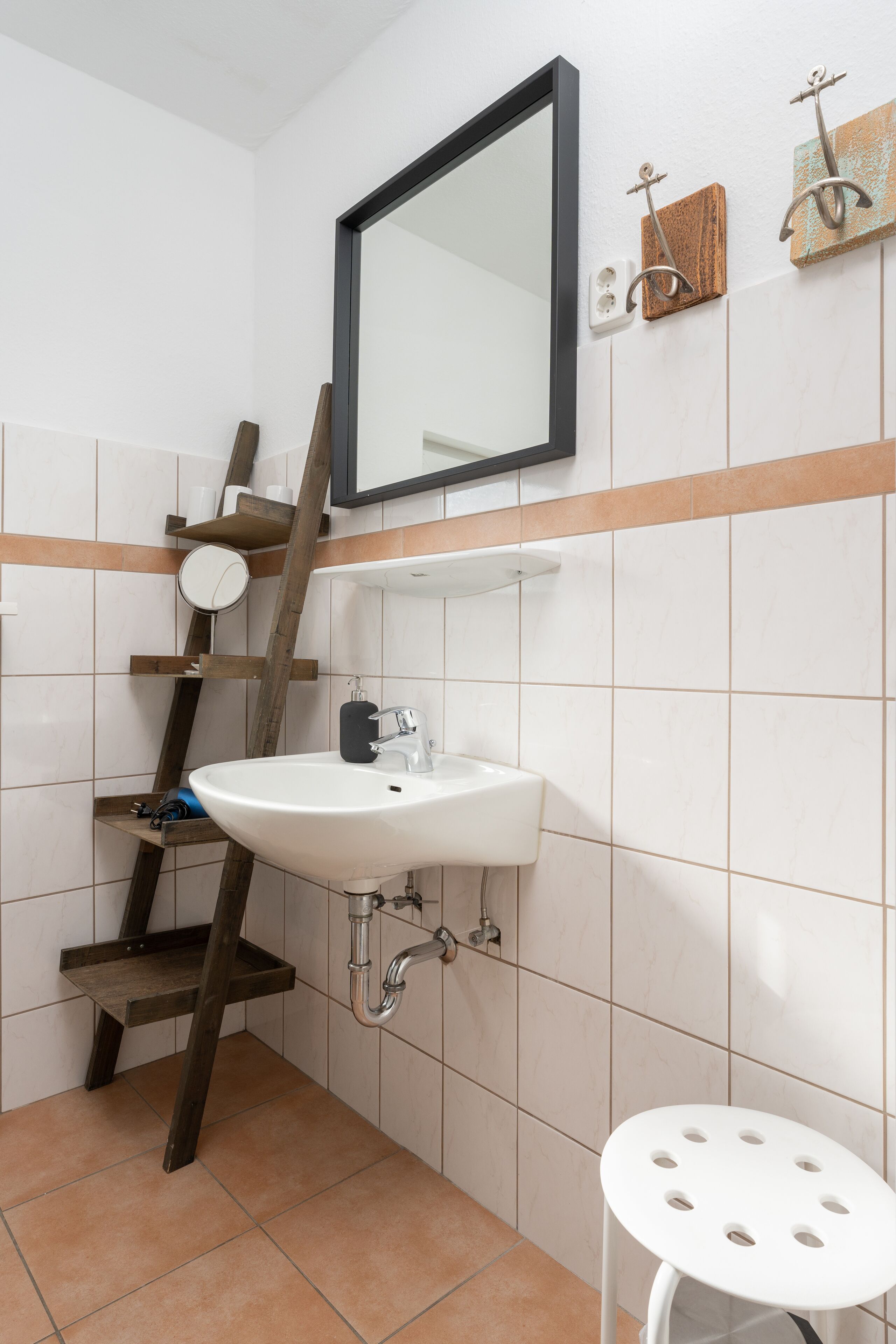 A bathroom with a white sink, a mirror, and a wooden ladder shelf.