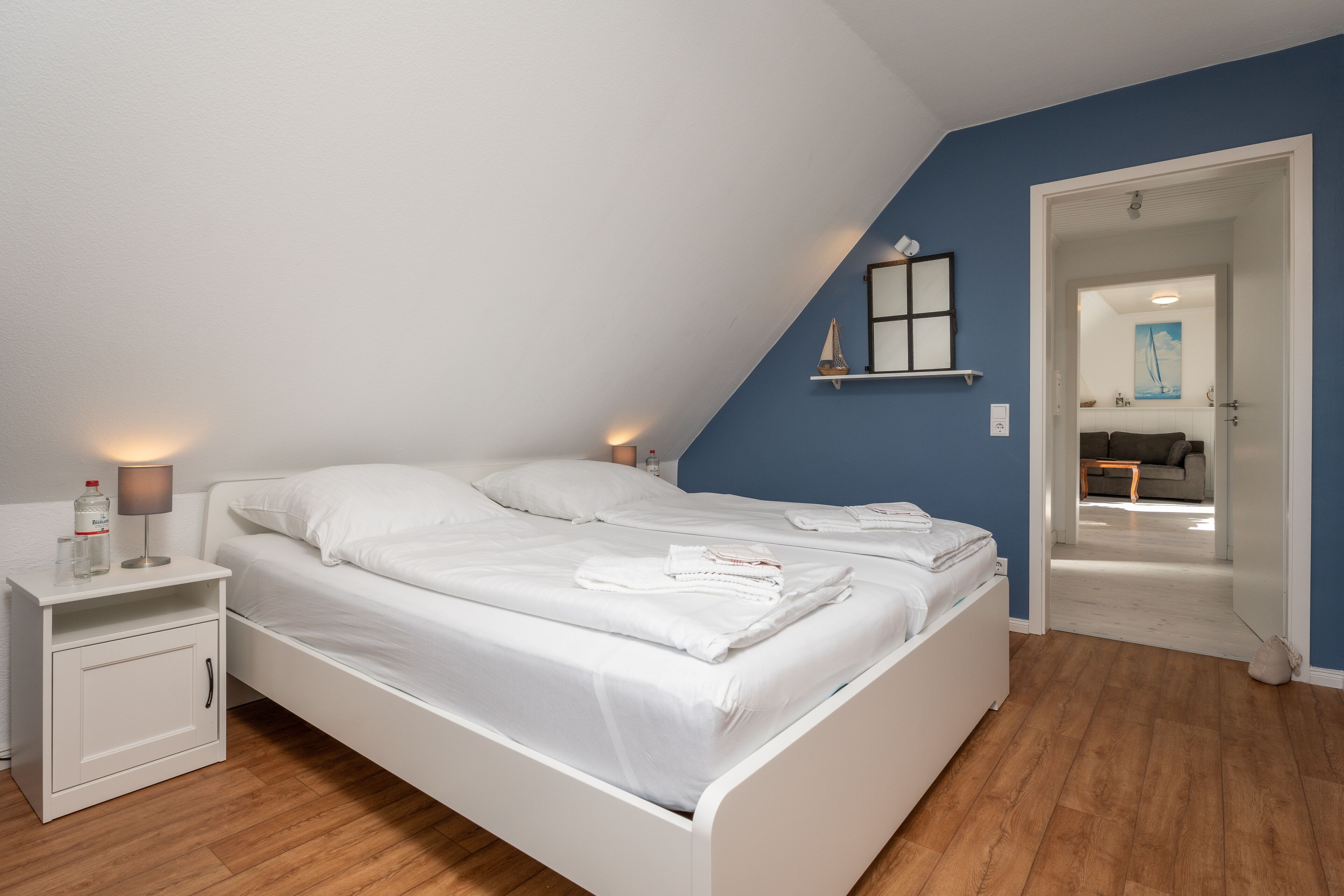 A bedroom with a white bed, a nightstand, a lamp, and a blue wall.