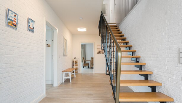 A staircase with wooden steps and a metal railing, leading to a room with white brick walls and a wooden floor. - Ferienwohnungen Haus Schau ins Land (Emmelsbuell-Horsbuell)