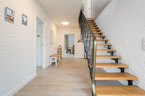 A staircase with wooden steps and a metal railing, leading to a room with white brick walls and a wooden floor.