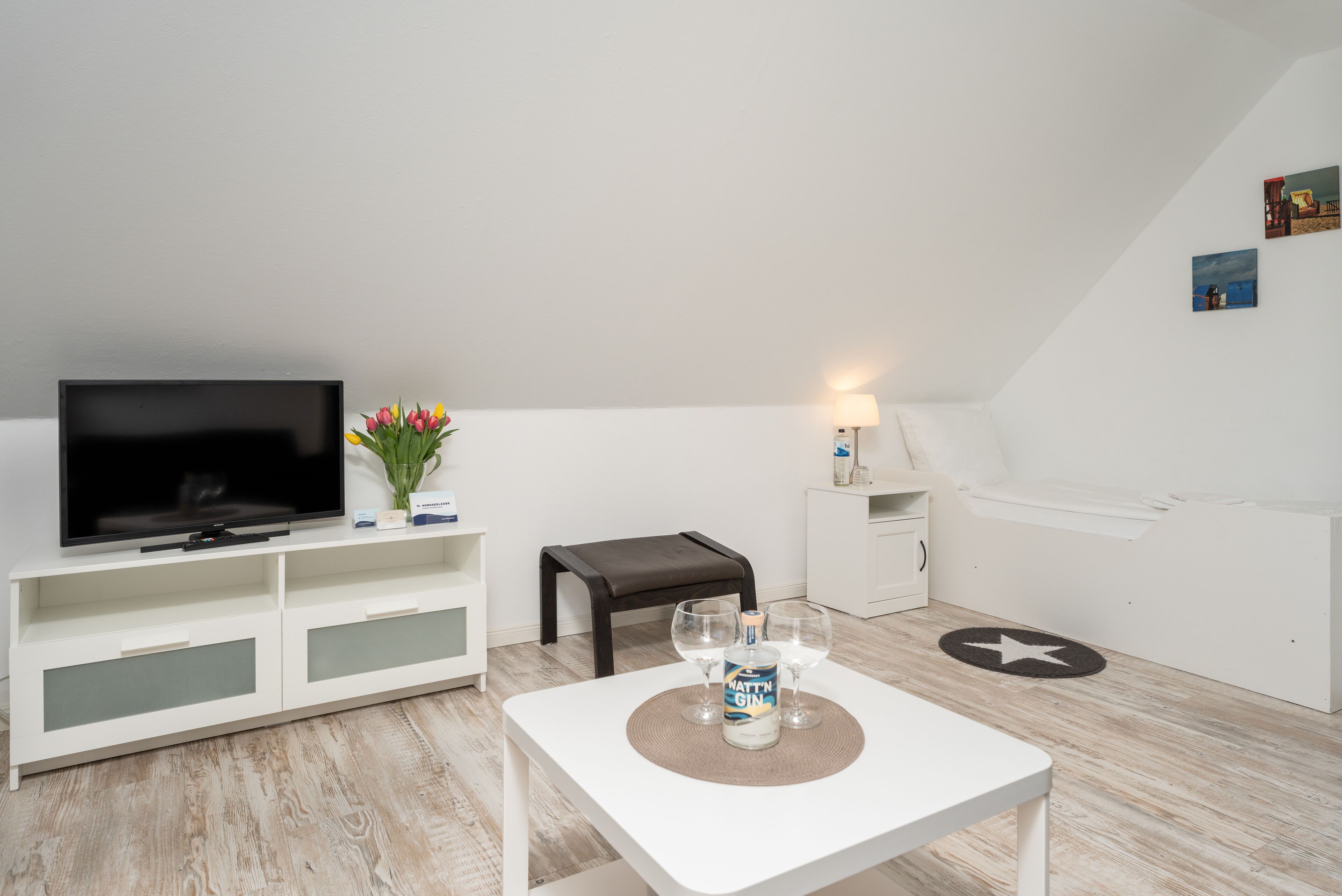 Ein modernes, minimalistisches Wohnzimmer mit einem Flachbildfernseher, einem kleinen Tisch mit einer Gin-Flasche und einer Bank.