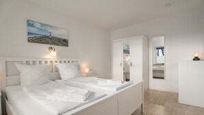 A modern bedroom with a large bed, bedside lamps, a wardrobe, and a painting of a lighthouse. - Ferienwohnungen Haus Schau ins Land (Emmelsbuell-Horsbuell)