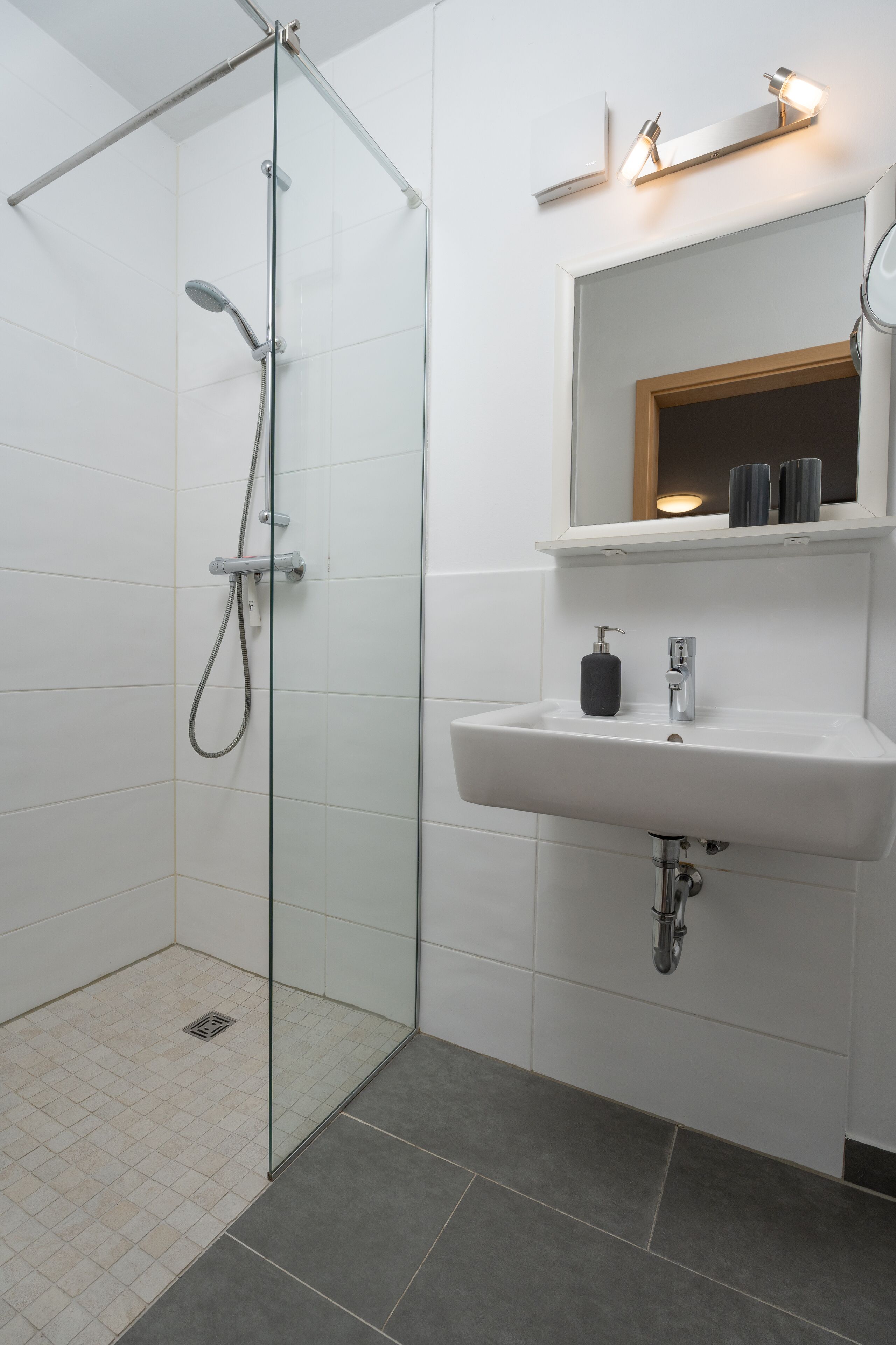 Ein modernes Badezimmer mit einer gläsernen Dusche, einem weißen Waschbecken und einem Spiegel darüber.