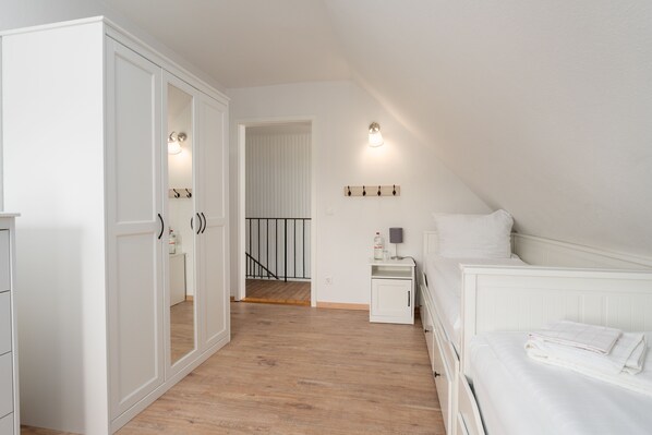 A bedroom with a white bed, a nightstand, a wardrobe, and a mirror. There is a staircase leading to another room.