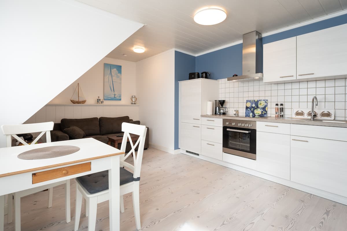 Une cuisine moderne avec des meubles blancs, un four encastré et un coin repas comprenant une table et des chaises blanches.