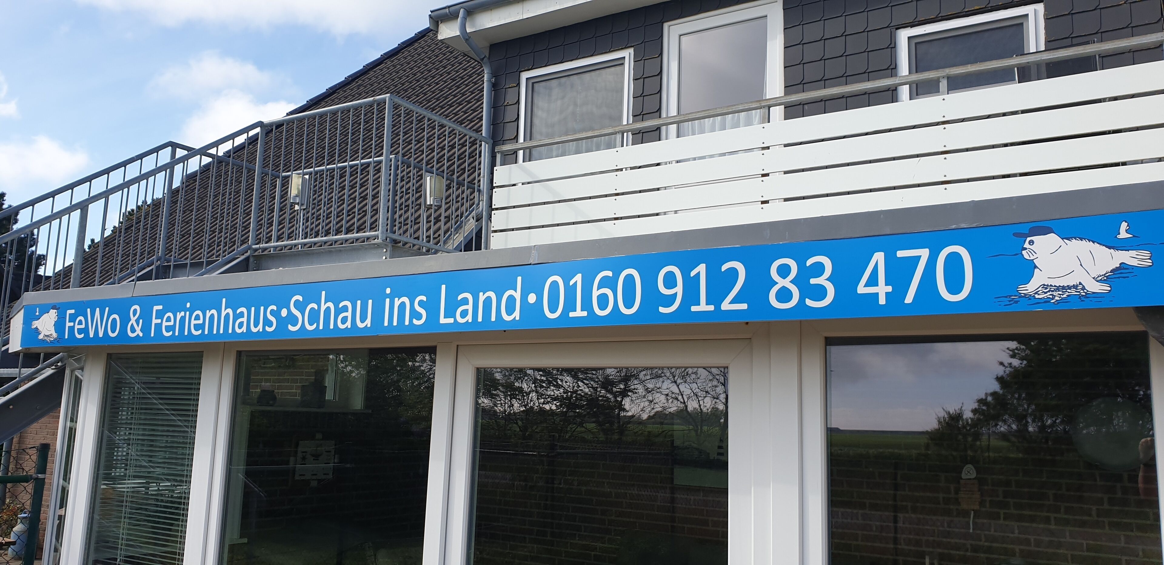 A blue sign with white text for 'FeWo & Ferienhaus' and a phone number.