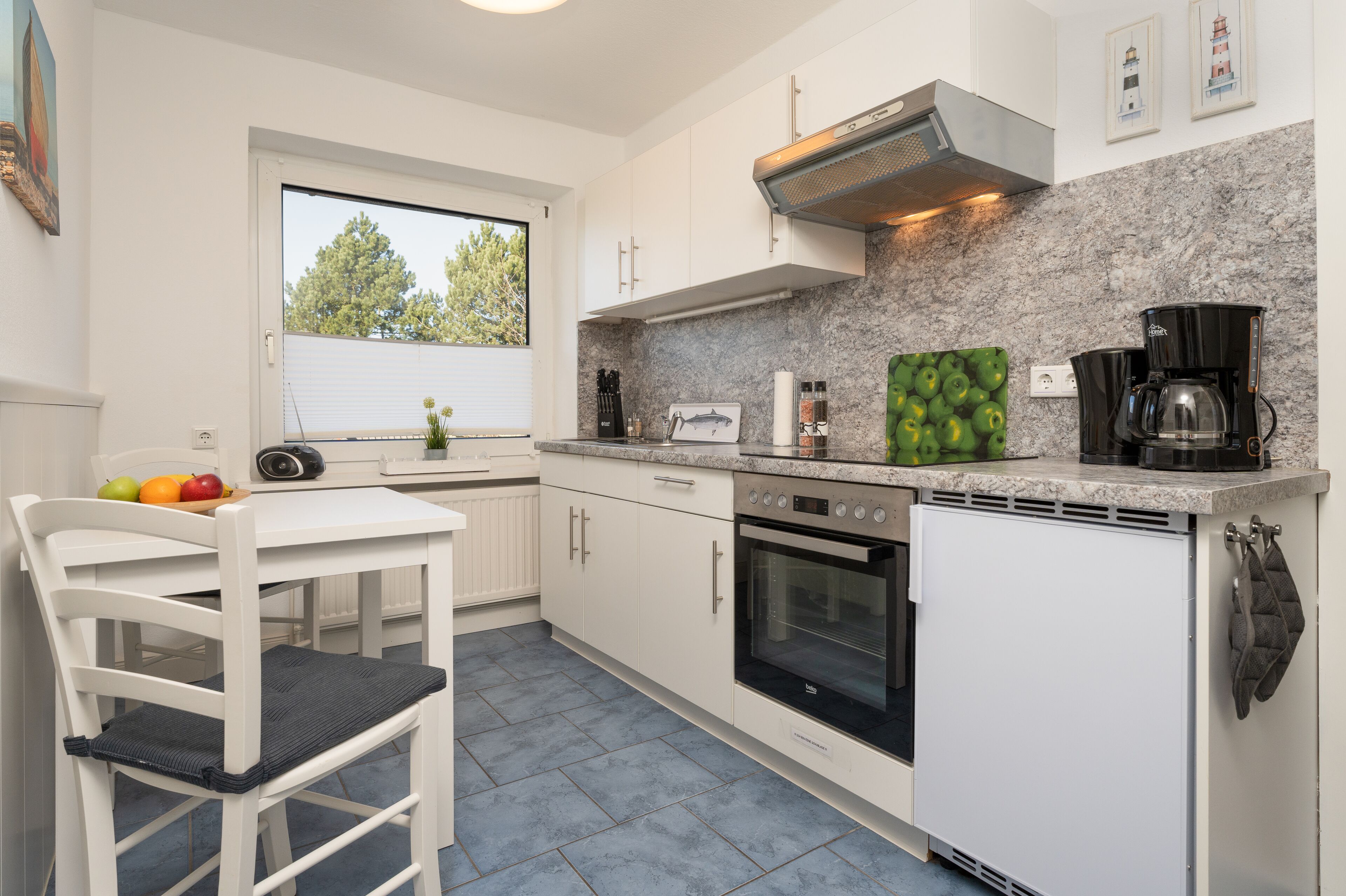 A modern kitchen with white cabinets, a built-in oven, a coffee maker, and a window with a view of trees.
