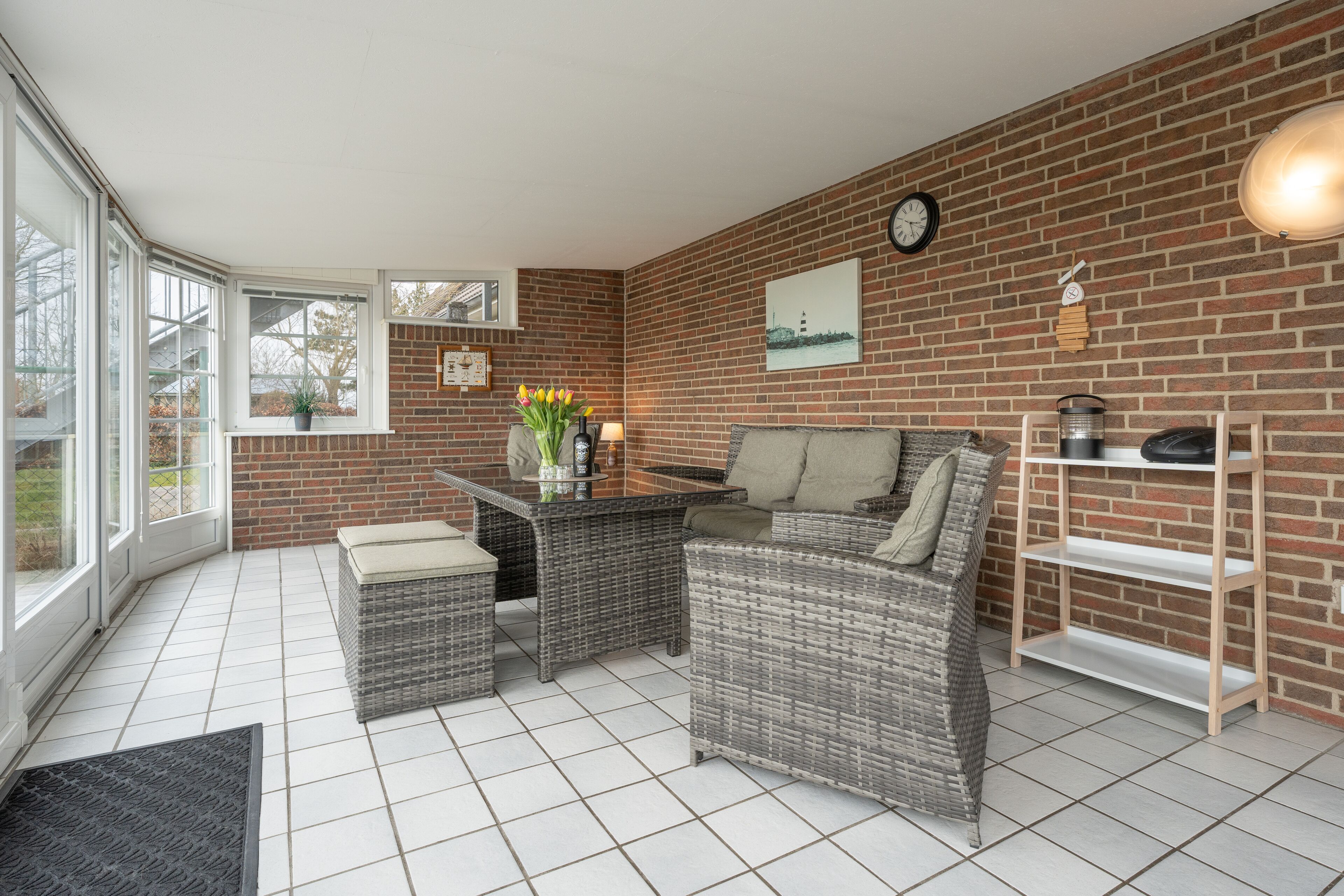 A room with a brick wall, wicker furniture, a tiled floor, and a view through a glass door.