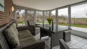 A sunroom with wicker furniture, large windows, and a view of the outdoors. - Ferienwohnungen Haus Schau ins Land (Emmelsbuell-Horsbuell)