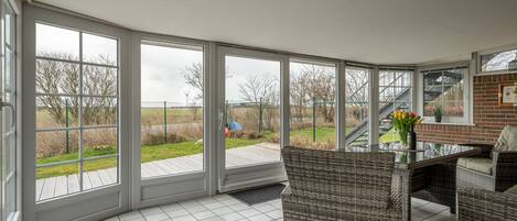 A sunroom with large windows, wicker furniture, and a view of a grassy area.