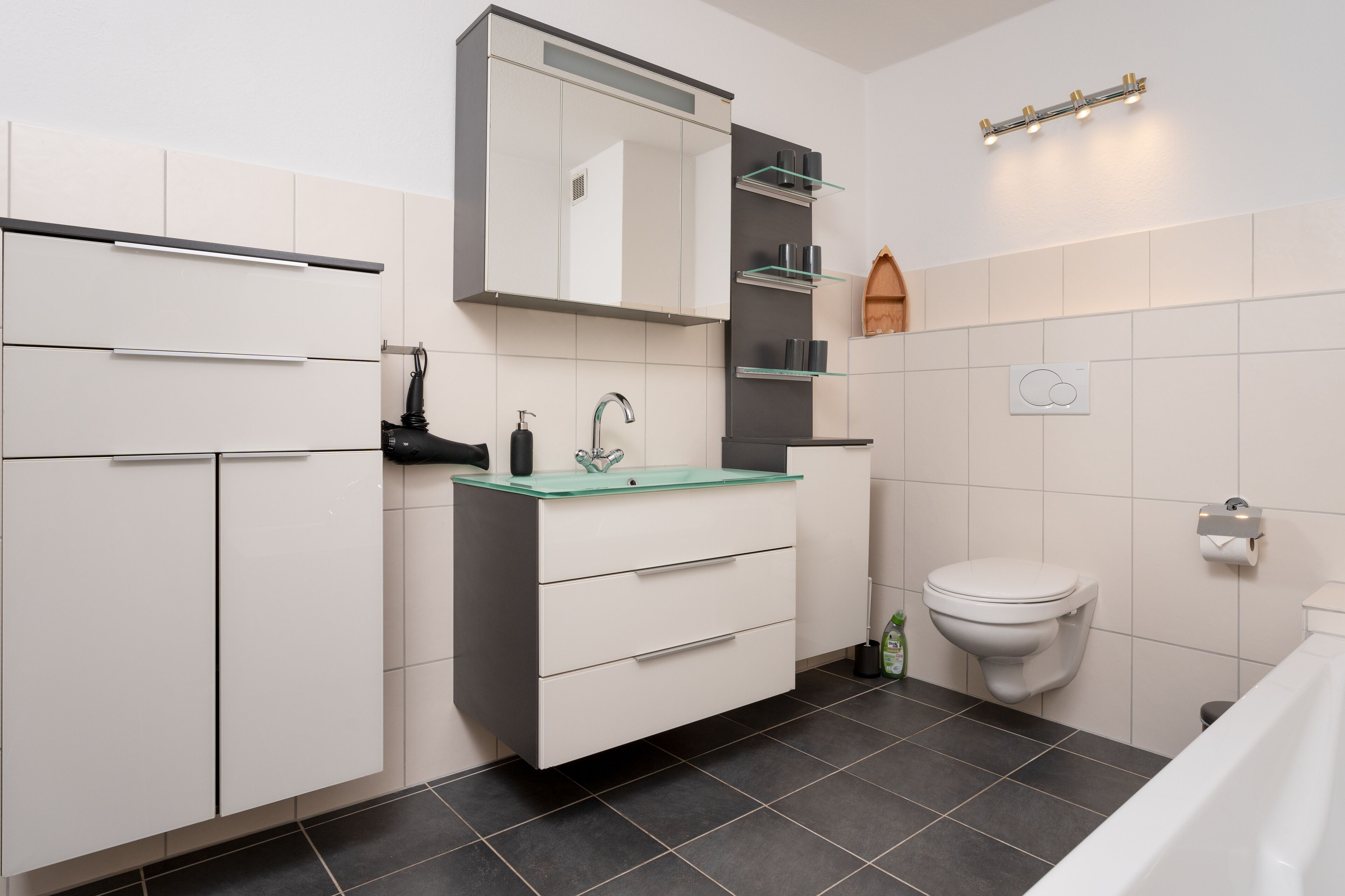A modern bathroom with a white vanity, a glass sink, a toilet, and a shower area.