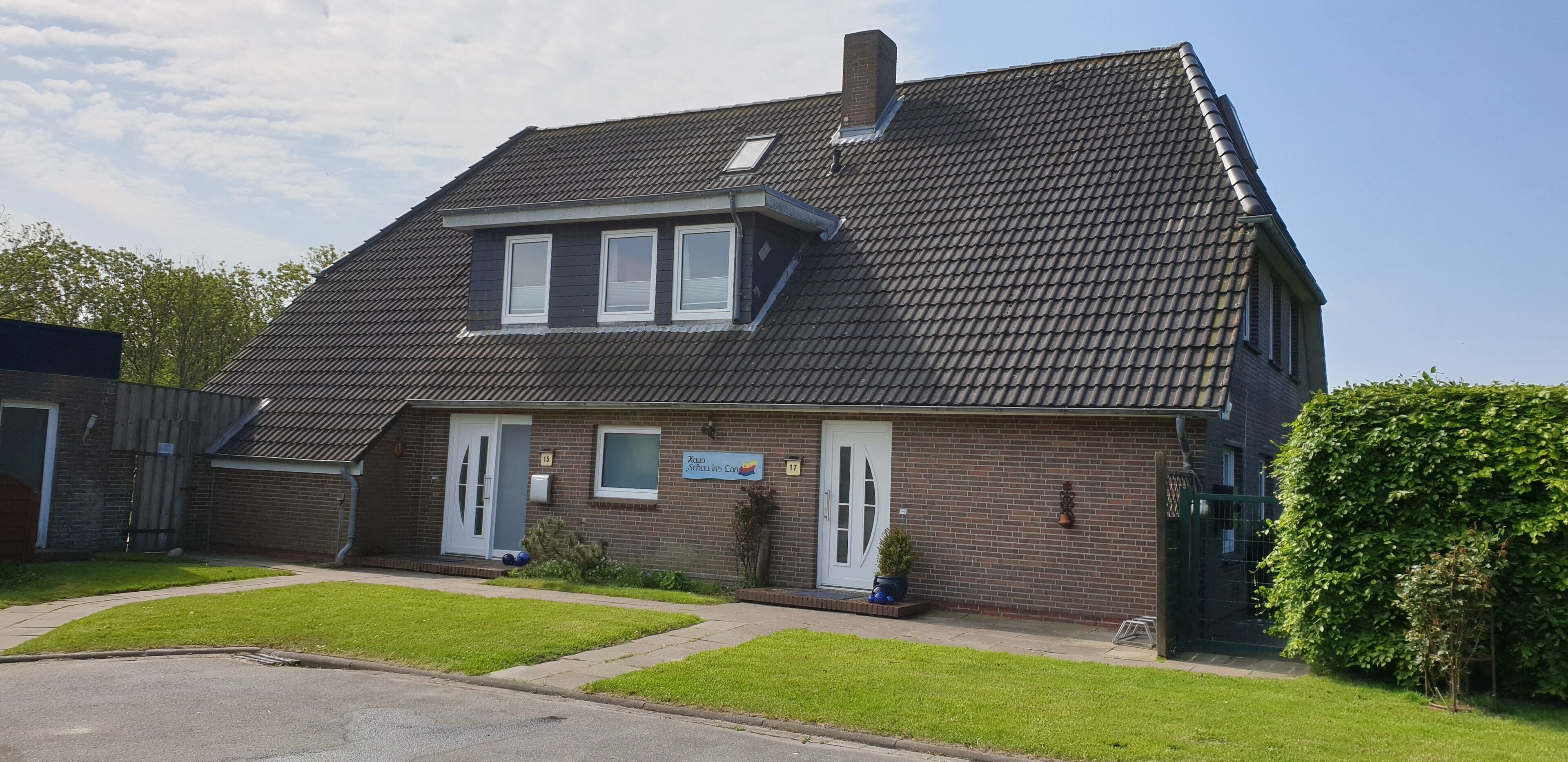 Une maison à deux étages, dotée d’un toit en pente, d’un porche à l’avant et d’un petit jardin.