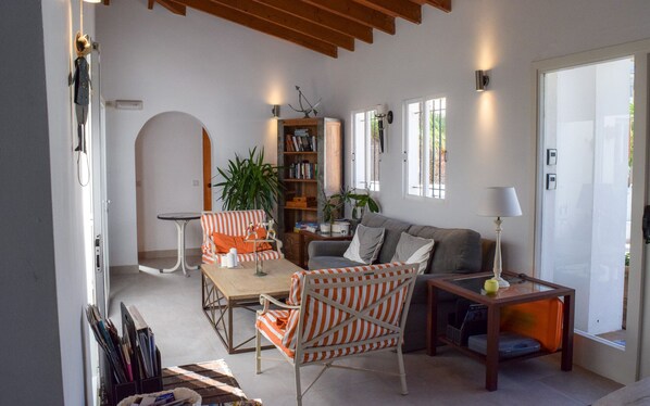 Un salon chaleureux avec un canapé, un fauteuil à rayures et une petite table sur laquelle se trouve une lampe. On y trouve également une bibliothèque remplie de livres et une plante en pot.