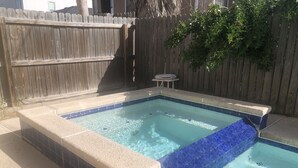 Un jacuzzi rectangular con borde de azulejos, rodeado por un cerco de madera y una pequeña mesa.
