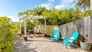 A patio area with a pergola, two turquoise chairs, a table, and a large planter. - The Dolphin Den- Blocks to the Beach and River~Kayaks and Bikes provided! (Cocoa Beach)