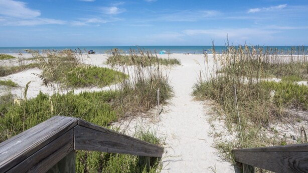 A sandy beach path leading to the ocean, surrounded by grass and a wooden fence. - The Dolphin Den- Blocks to the Beach and River~Kayaks and Bikes provided! (Cocoa Beach)