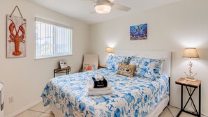 A bedroom with a bed, a ceiling fan, a window, a nightstand, and a lamp. - The Dolphin Den- Blocks to the Beach and River~Kayaks and Bikes provided! (Cocoa Beach)