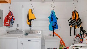 A laundry area with a washing machine, dryer, and a rack with various garments and a life jacket. - The Dolphin Den- Blocks to the Beach and River~Kayaks and Bikes provided! (Cocoa Beach)