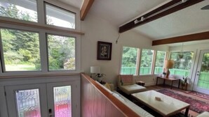 A spacious living room with a high ceiling, large windows, and a view of greenery outside. - Private mid-century modern hideaway in forest near the river and sea. (Crescent City)