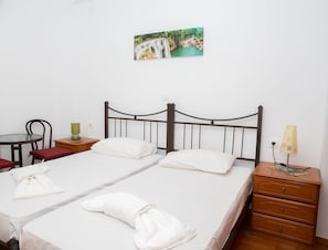 Une chambre d’hôtel avec deux lits, une petite table, une chaise, une table de chevet avec une lampe et un tableau au mur.
