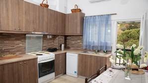 A modern kitchen with wooden cabinets, a dishwasher, and a dining area with a table set for two. - White Heaven. Near the Marina Lakki and a Wonderful View of the Port. (Leros)