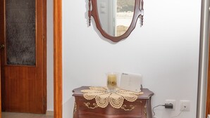 A room with a wooden door, a mirror, a small table with a lace tablecloth, and a white device on the table. - White Heaven. Near the Marina Lakki and a Wonderful View of the Port. (Leros)