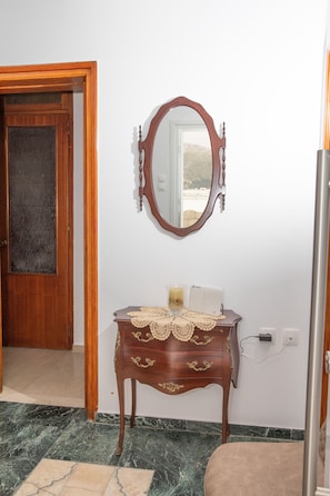 Une pièce avec une porte en bois, un miroir, une petite table recouverte d’une nappe en dentelle et un appareil blanc posé sur la table.