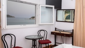 A hotel room with a bed, a small table, two chairs, a TV, and a window with a view of the sea. - White Heaven. Near the Marina Lakki and a Wonderful View of the Port. (Leros)