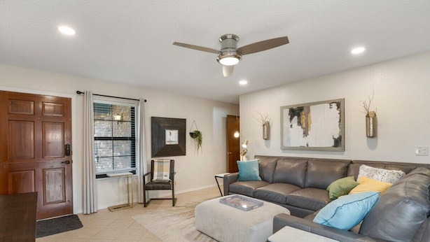 A living room with a sofa, ottoman, and a ceiling fan. - Jenks Spectacular Spain Ranch-Close to Five Oaks (Jenks)