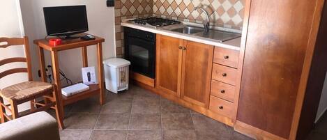 A compact kitchen with wooden cabinets, a gas stove, a sink, and a small dining area with a chair and a table.