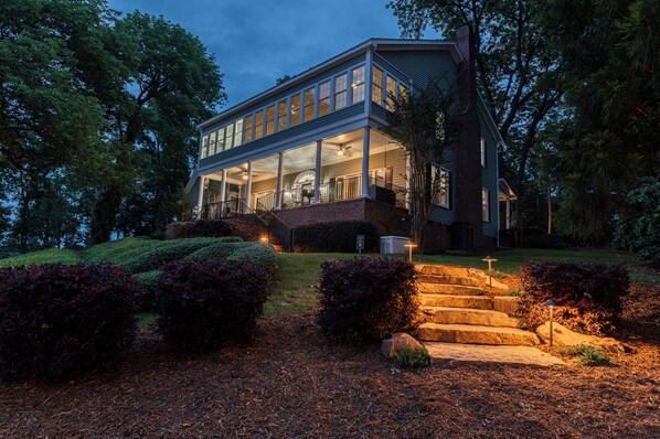 A modern two-story house with a large glass front, a covered porch, and a stone staircase leading to the entrance.