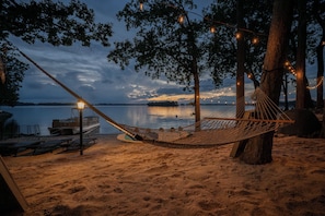A hammock on a sandy beach with a boat and a dock in the background.