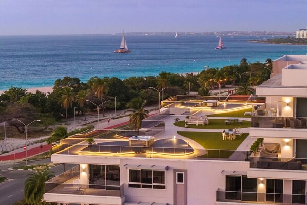 Ein modernes Hotel mit Dachterrasse, Schwimmbad und Blick auf das Meer mit Segelbooten.