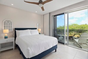 Ein modernes Schlafzimmer mit einem großen Bett, zwei Nachttischen mit Lampen, einem Deckenventilator und einem Balkon mit Sitzgelegenheiten.