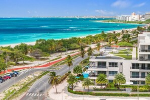 Ein Hotel am Meer mit modernem Design, das eine Zufahrt zum Strand, Palmen und einen Blick auf den Ozean zeigt.