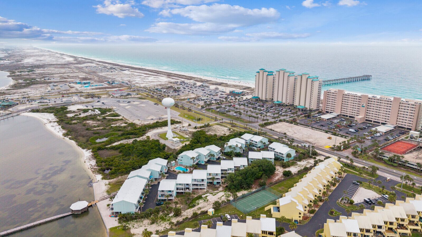 Vue aérienne d’une station balnéaire avec des villas en bord de mer, une plage et une jetée.