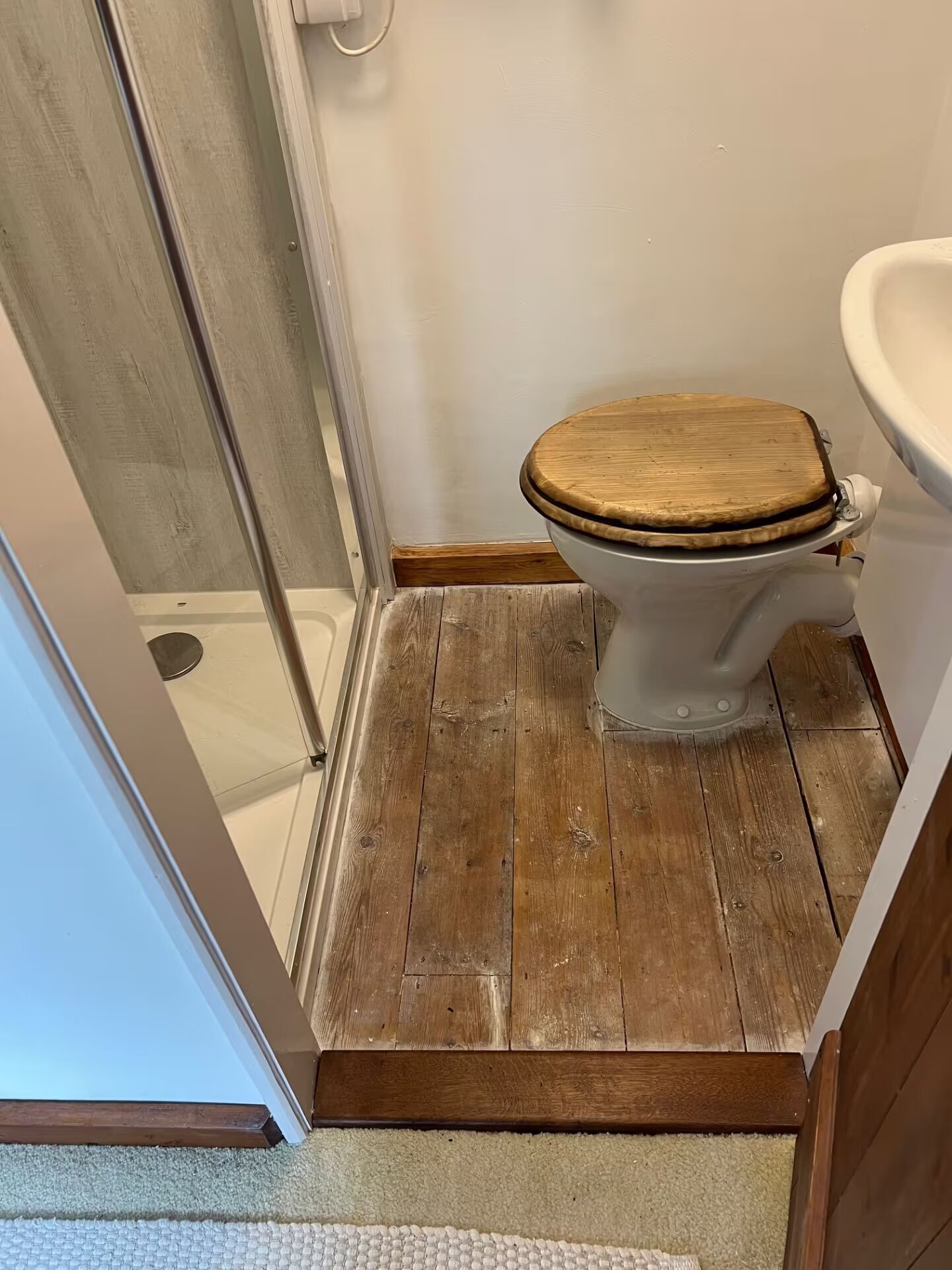 A bathroom with a wooden floor, a white toilet, and a shower area.