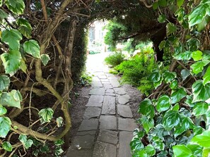 A stone pathway surrounded by lush greenery and a tree arching over it. - Dog-friendly, Secluded, Spacious Cottage with Large Garden. Sleeps 6 (Woodbridge)