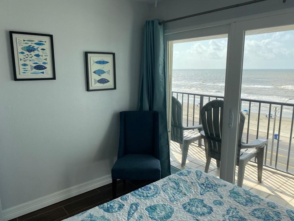 A room with a bed, a chair, and a balcony with a view of the ocean.