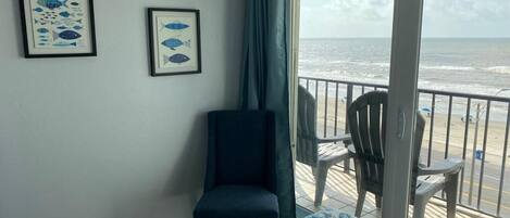 A room with a bed, a chair, and a balcony with a view of the ocean.