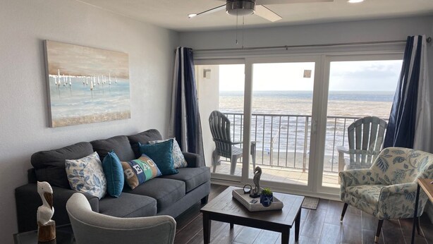 A living room with a sofa, chairs, a coffee table, and a view of the ocean through large sliding doors. - Galveston Oceanview,Wonderful location! 2bed/2bath (Galveston)