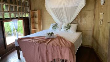 Quarto com cama, dossel, prateleira de madeira e janela com vista para o verde.