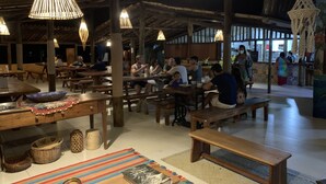 A restaurant with wooden tables and benches, hanging light fixtures, and a tiled floor. - Unah Piracanga (Maraú)