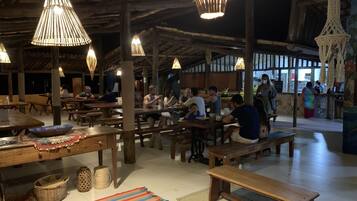 Um restaurante com mesas e bancos de madeira, luminárias pendentes e piso de azulejos.