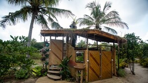 A wooden structure with a wooden door and a small sink, surrounded by tropical vegetation. - Unah Piracanga (Maraú)