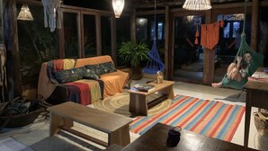A cozy living room with a sofa, a coffee table, and a hanging chair. - Unah Piracanga (Maraú)
