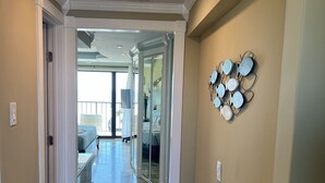 Un couloir doté d’un sol carrelé, d’un miroir décoratif fixé au mur et d’une porte donnant sur un balcon.