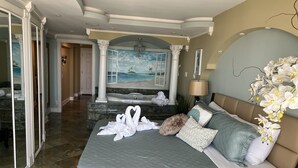 Une chambre spacieuse avec un grand lit, un jacuzzi et une vue sur la plage, accessible par une fenêtre ouverte.