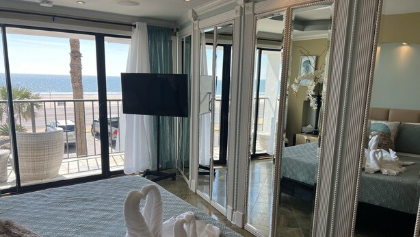 Une chambre d’hôtel avec un grand lit, une télévision, un balcon avec vue sur la mer et un grand miroir.