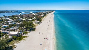 An aerial view of a coastal area with a beach, a marina, and a residential area with buildings and greenery. - Runaway Bay 283 by Duncan Real Estate (Bradenton Beach)